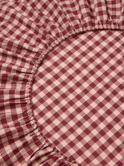 A close-up of a red and white gingham checkered sheet with a gathered elasticized edge.