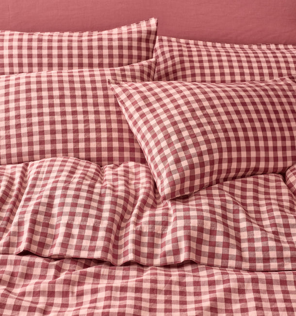 Red and light pink gingham check bedding set including a duvet cover and matching pillowcases, styled on a bed against a solid dusty rose wall.