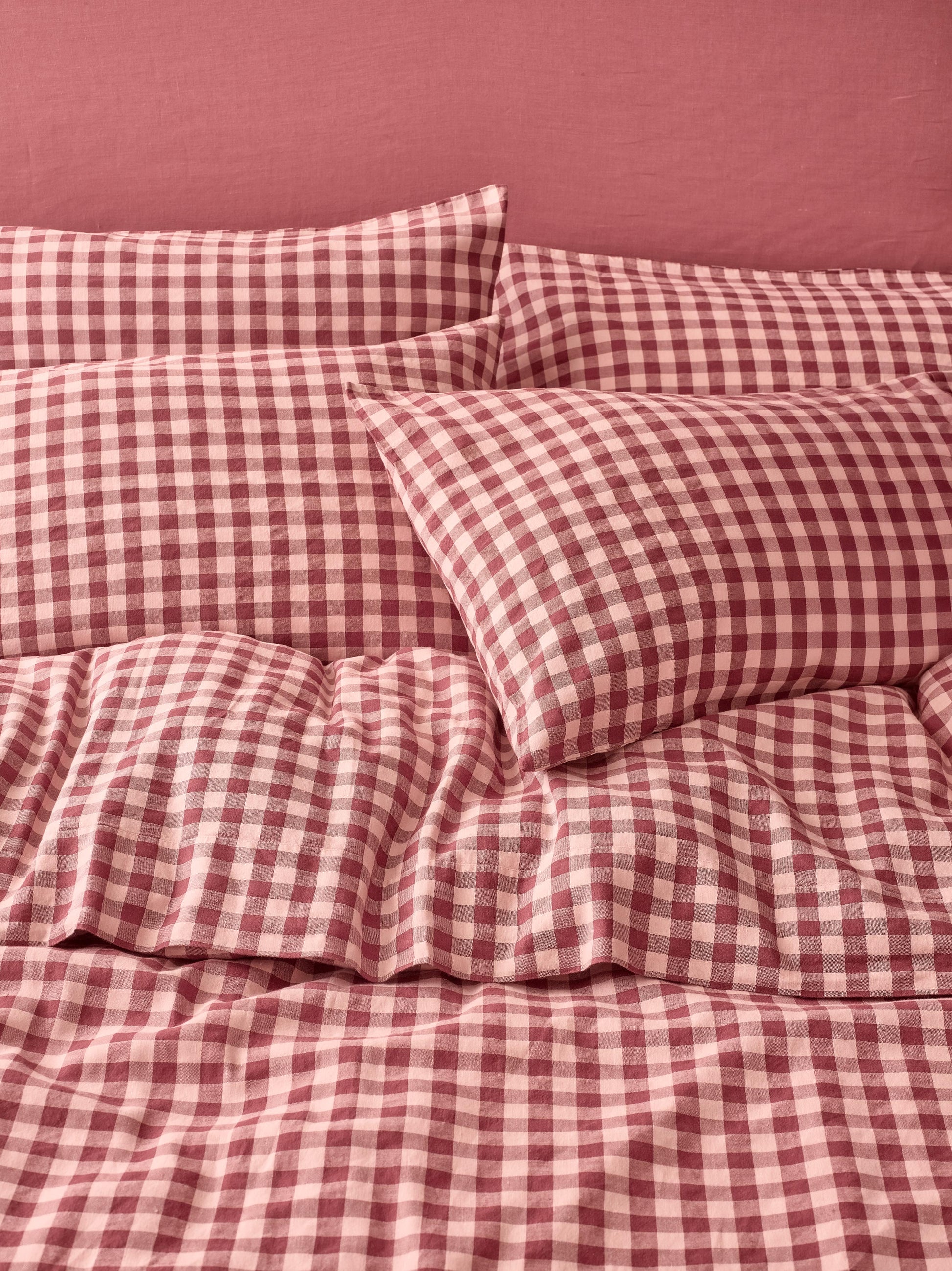 Red and light pink gingham check bedding set including a duvet cover and matching pillowcases, styled on a bed against a solid dusty rose wall.
