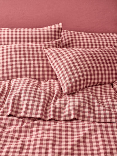 Red and light pink gingham check bedding set including a duvet cover and matching pillowcases, styled on a bed against a solid dusty rose wall.