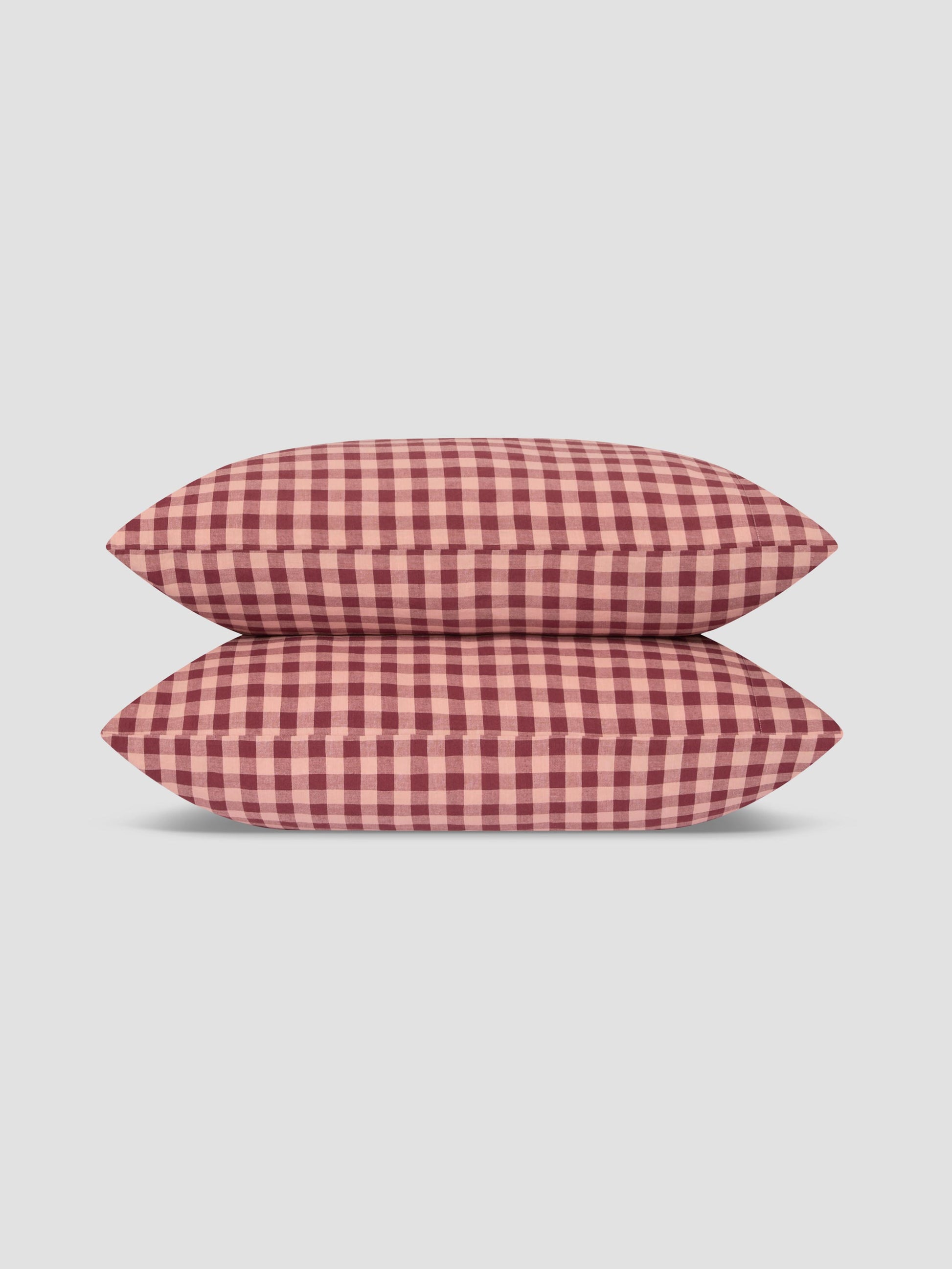 Two pillows stacked vertically, featuring a red and white gingham checkered pattern, set against a solid light gray background.