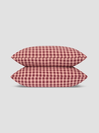 Two pillows stacked vertically, featuring a red and white gingham checkered pattern, set against a solid light gray background.