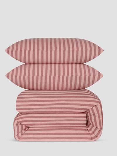 A stack of three pink and white striped bedding items, including two pillows and a folded duvet cover, shown on a light gray background.
