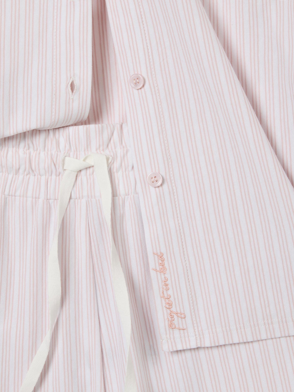 Close-up of a light pink and white striped pajama set with a drawstring waist and a small embroidered brand name on the sleeve.