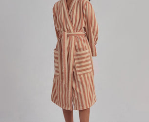 A woman modeling a long-sleeved striped bathrobe with a matching waist tie, standing against a plain light gray studio background.