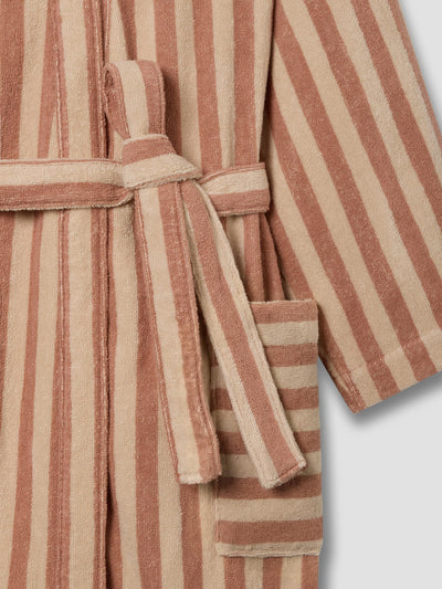 A close-up of a striped bathrobe made of soft terry cloth, featuring alternating vertical stripes in terracotta and beige, with a matching tie belt and a side pocket.