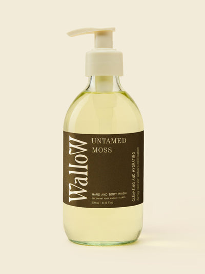 A 300ml pump bottle of Wallow Untamed Moss hand and body wash, filled with a pale yellow liquid, set against a solid cream background.