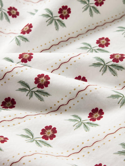 Close up of a white fabric with subtle red stripes and red floral print. 