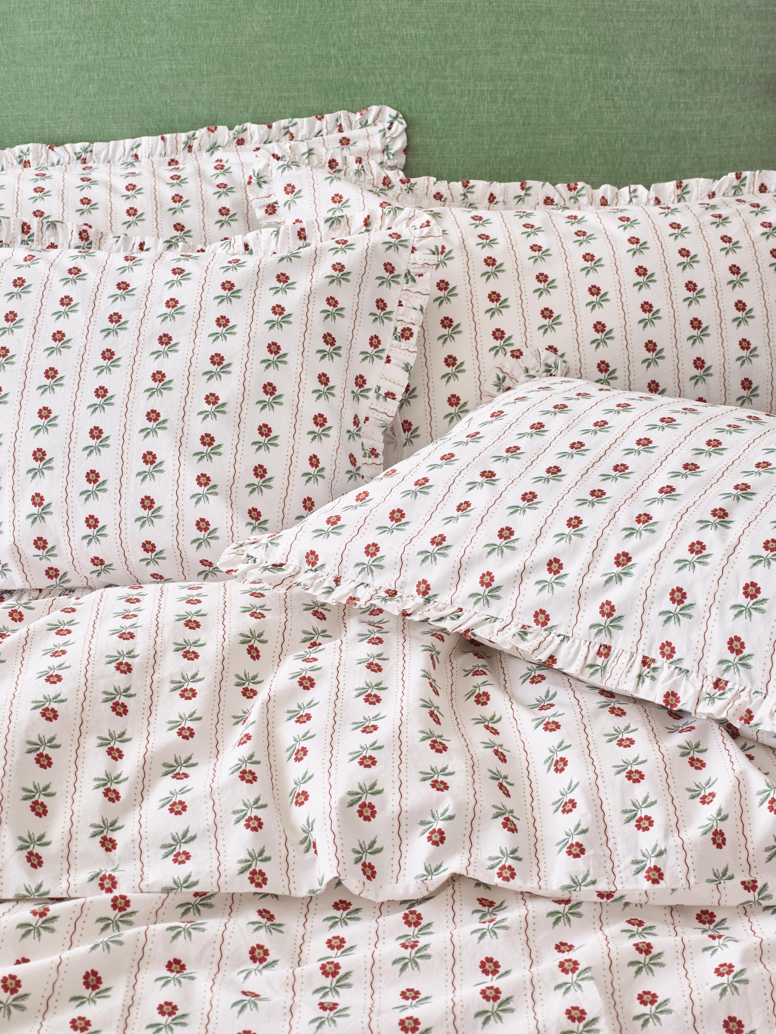 White bedding with red floral print and frilled edges on the pillows, set on a green background