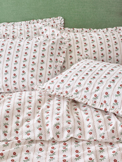 White bedding with red floral print and frilled edges on the pillows, set on a green background