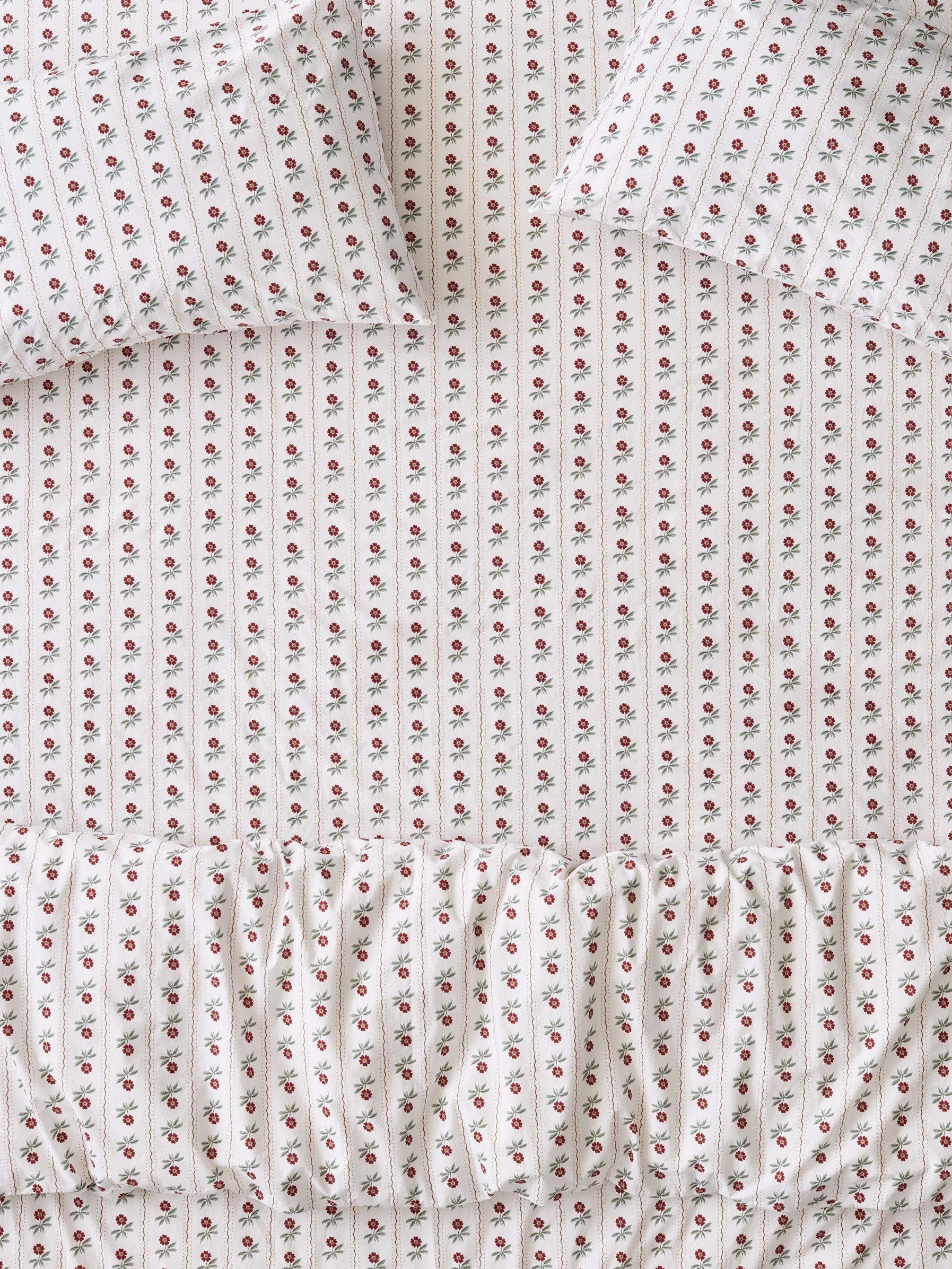Close-up of a white bed set with a delicate repeating pattern of small pink and red flowers with green leaves.