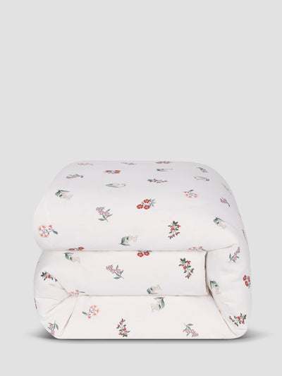 White comforter with subtle colourful print, folded on a grey background. 