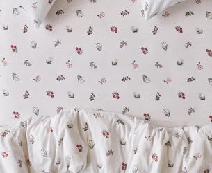 Close up of a bed with fitted sheet, pillowcases and duvet cover in a white fabric with a subtle floral print. 