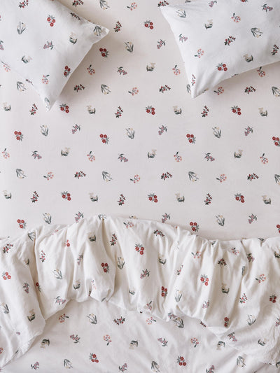 Close up of a bed with fitted sheet, pillowcases and duvet cover in a white fabric with a subtle floral print. 
