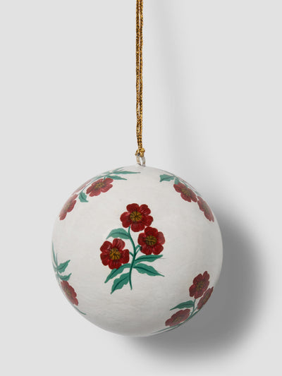 A white spherical ornament with a hand-painted floral pattern of red flowers and green leaves, hanging from a gold string against a light gray background.