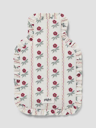 A hot water bottle cover featuring an off-white background with vertical stripes of red flowers and green leaves, finished with a ruffled edge.
