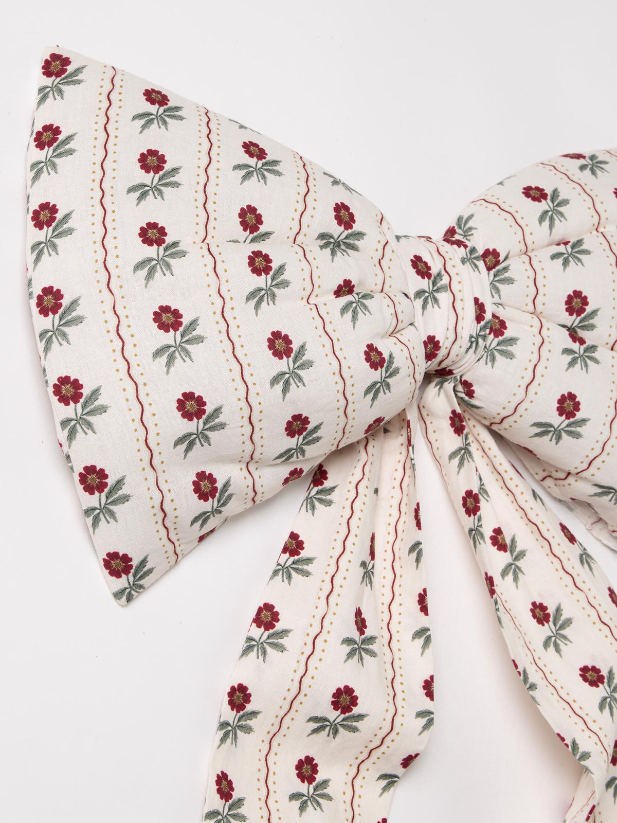 A fabric bow featuring an off-white background with vertical wavy red lines and small red flowers with green leaves, tied in the center.