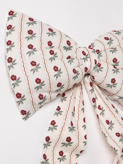 A fabric bow featuring an off-white background with vertical wavy red lines and small red flowers with green leaves, tied in the center.