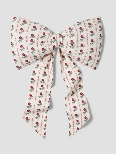 A large bow-shaped hair accessory made of cream-colored fabric with a repeating pattern of small red roses and green leaves, tied in the center and hanging down, shown against a solid light gray background.