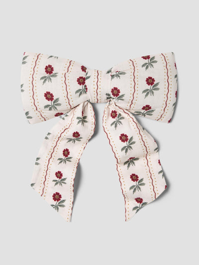 A fabric bow with a cream background, featuring vertical stripes of red flowers with green leaves and red dotted lines, set against a solid light gray background.