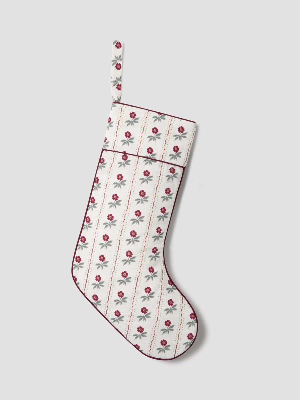 A Christmas stocking with a white background, decorated with a repeating pattern of red roses and green leaves, finished with dark red piping and a hanging loop.