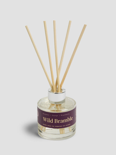 Diffuser with reeds with a burgundy label reading "Wild Bramble", on a light grey background. 