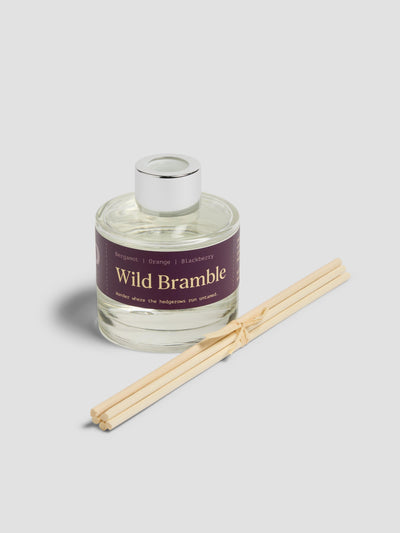 Diffuser with reeds with a burgundy label reading "Wild Bramble", on a light grey background. 